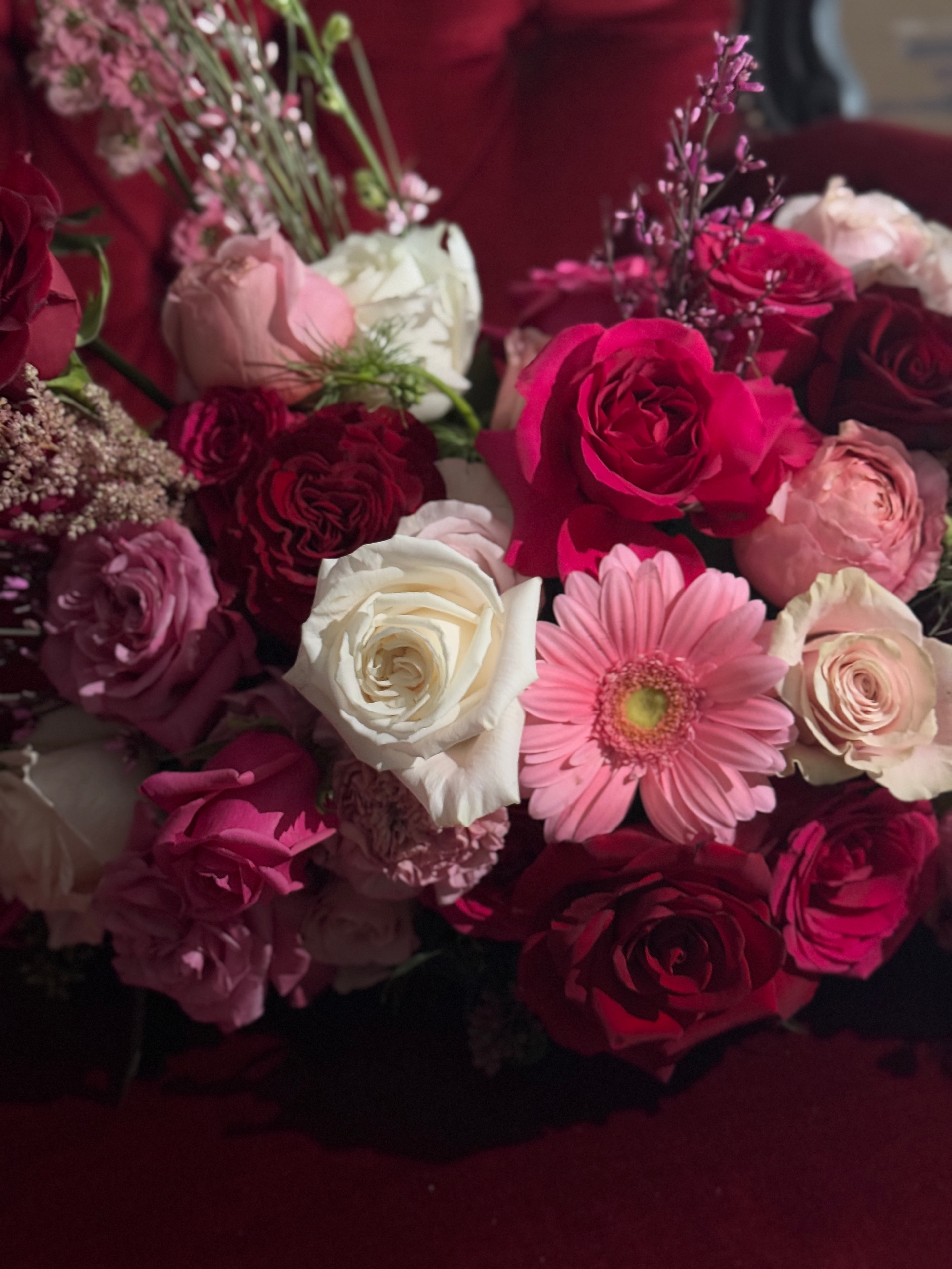 Lush quinceañera floral arrangement with deep red roses, hot pink roses, white roses, pink gerberas, and lavender blooms