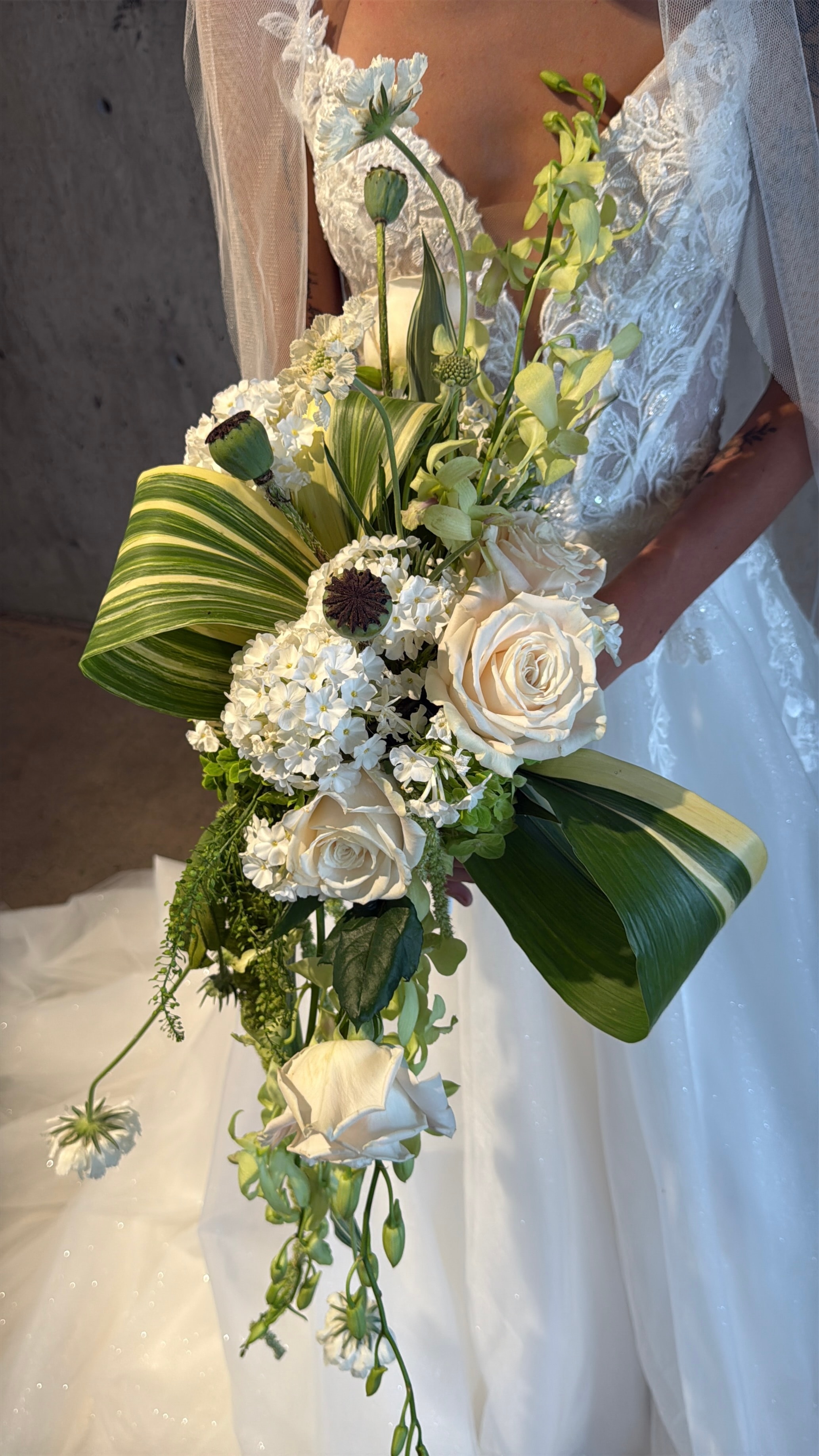 Bride holding dramatic burgundy and dahlia bouquet by water fountain