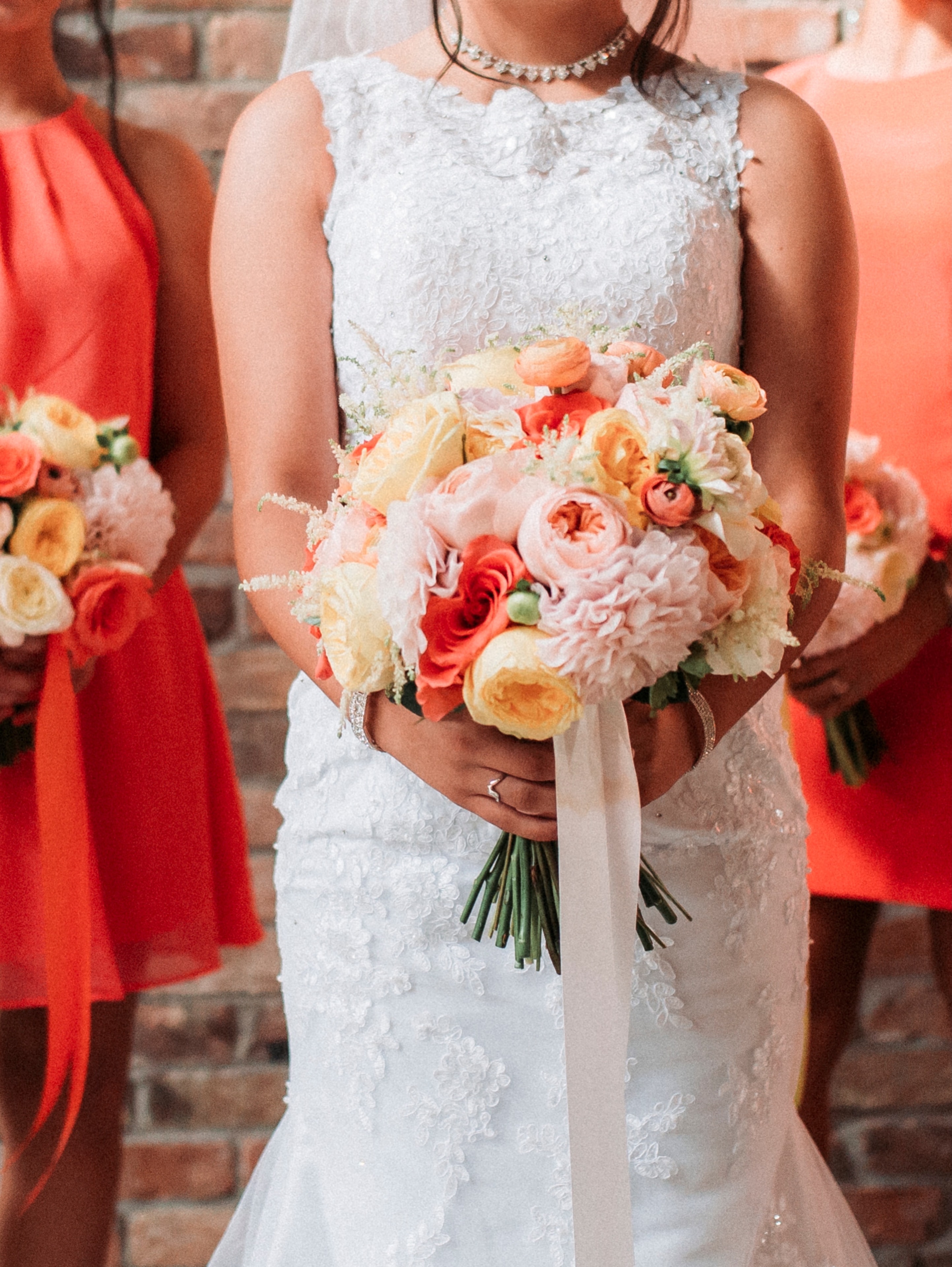 Bride with coral, peach, and blush bouquet with bridesmaids in orange